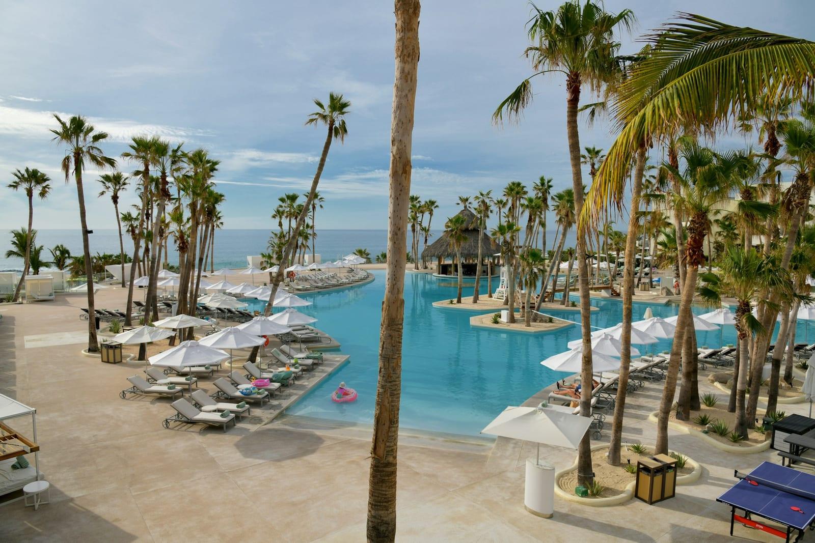 Resort pool deck lined with palm trees at a beachfront all-inclusive property in Los Cabos, Mexico
