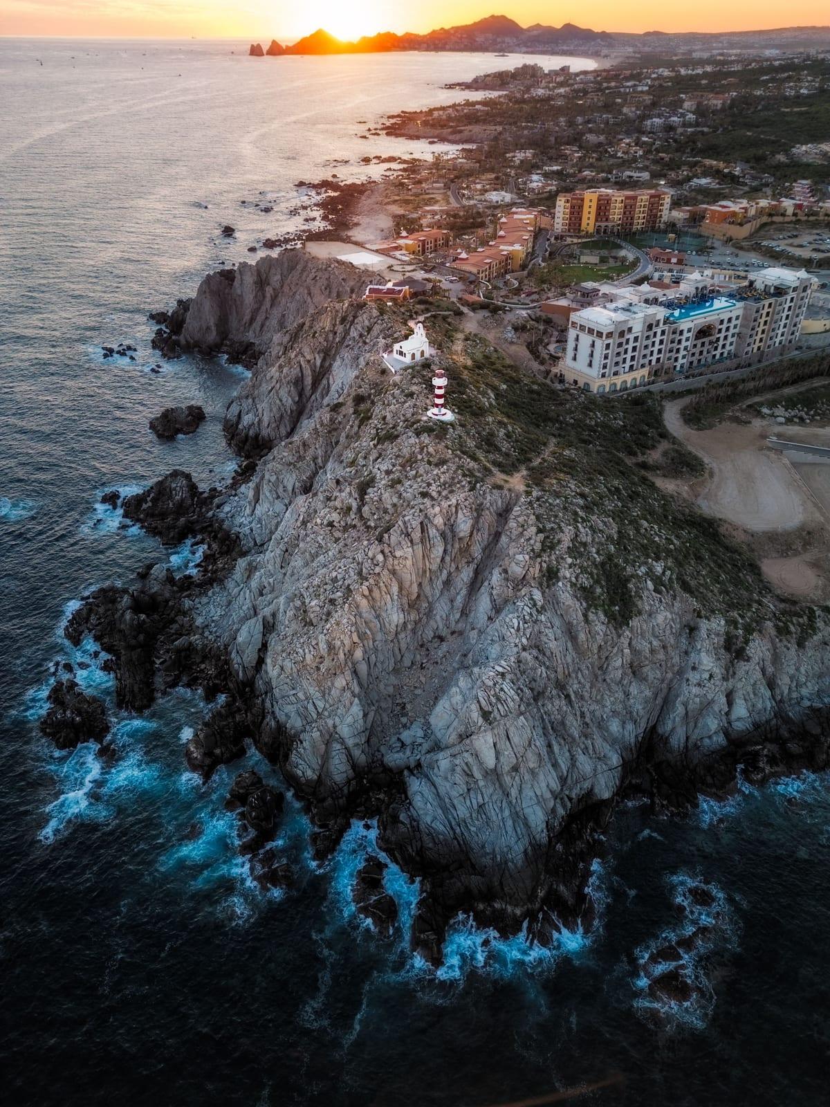 Aerial view of rocky cliffs and a lighthouse along the San José del Cabo coastline at sunset