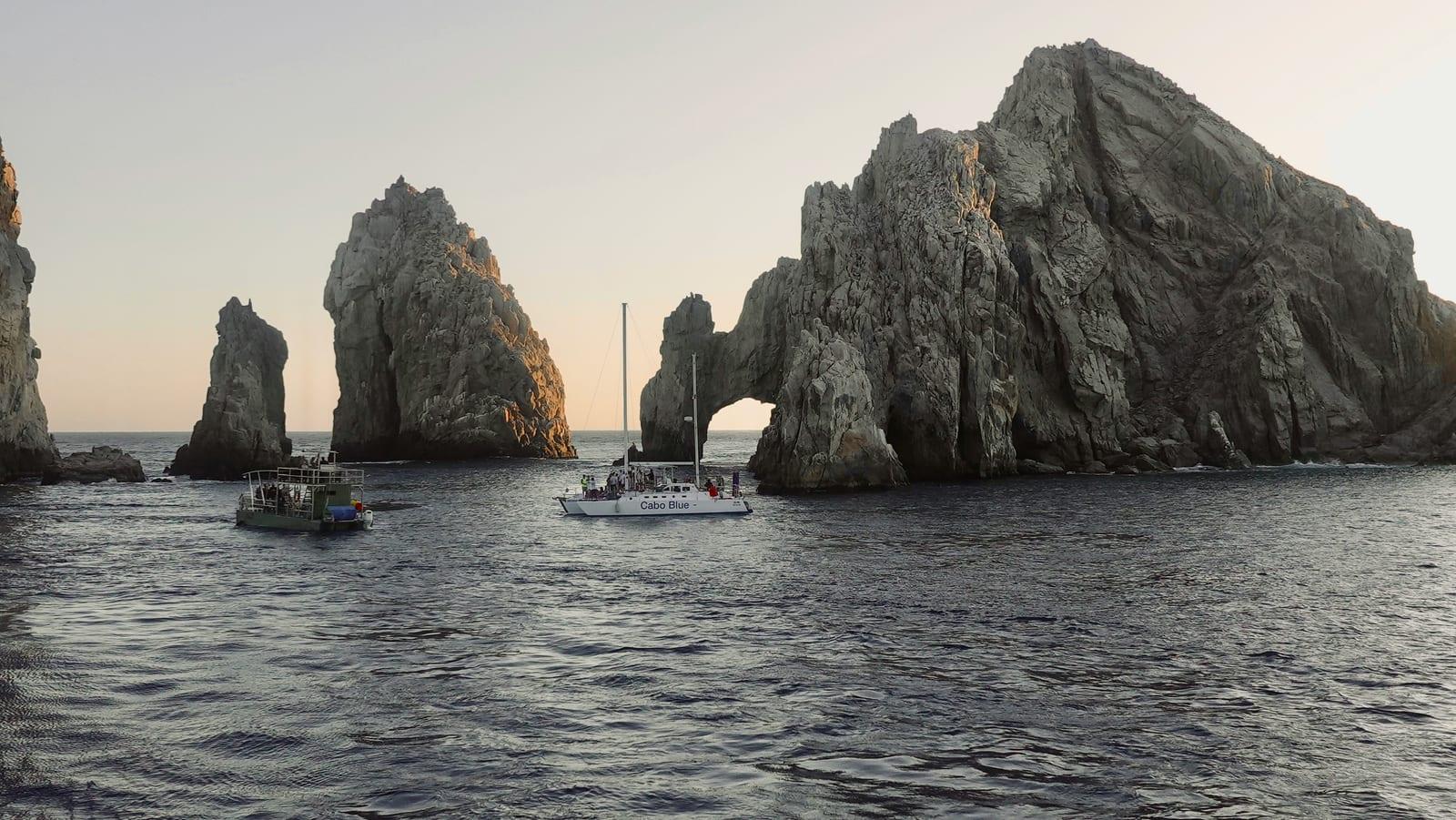 A tour catamaran and panga anchored beside the Arch of Cabo San Lucas at sunset