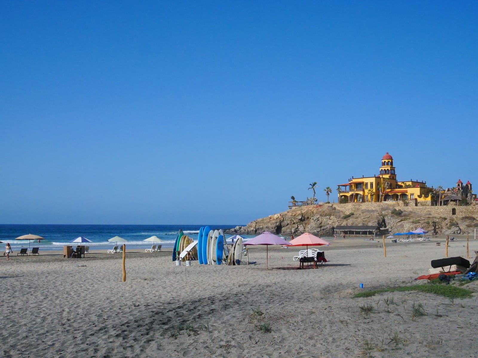 Cerritos Beach, a sandy Pacific surf beach near El Pescadero, with colorful beach umbrellas along the shore.