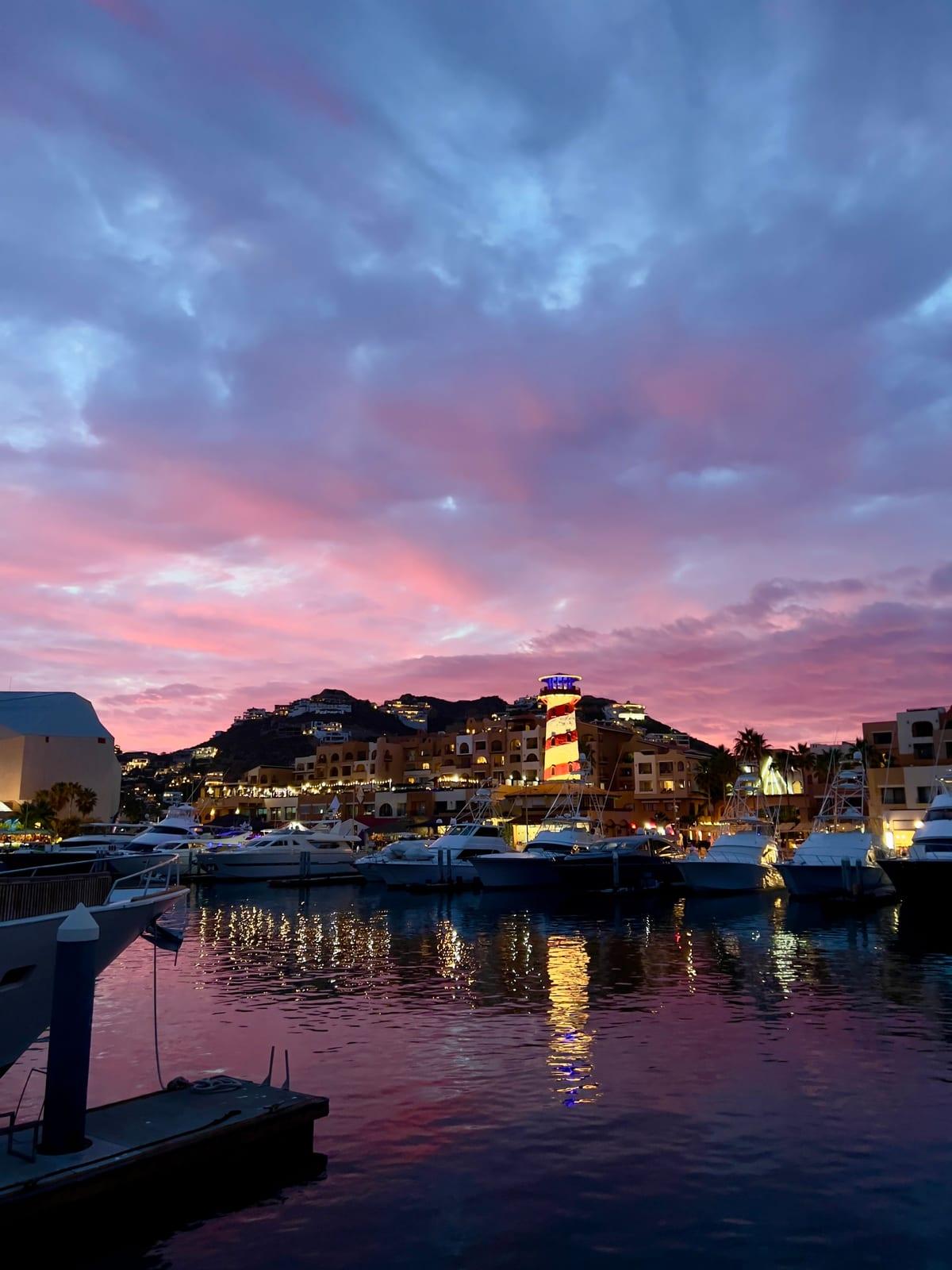 Sunset over the Cabo San Lucas marina, boats docked in front of the lit lighthouse tower